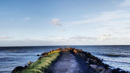 Narrow pathway leading to calm sea against sky