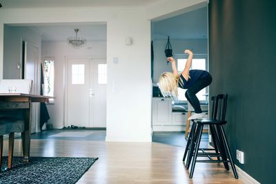 Side view of girl jumping from chair in living room at home