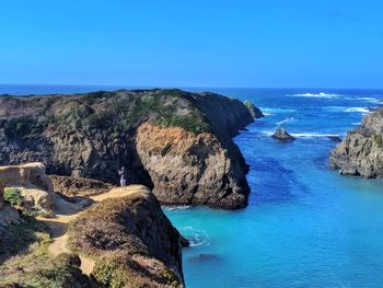 Scenic view of woman taking smartphone pictures on cliff overlooking ocean.