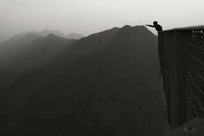 Optical illusion of man reaching mountain against sky