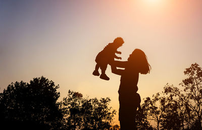 Silhouette mother lifting son against sky during sunset