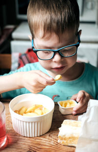 A boy in glasses eats french fries with cheese sauce, at home at the table. fast food for kids. 