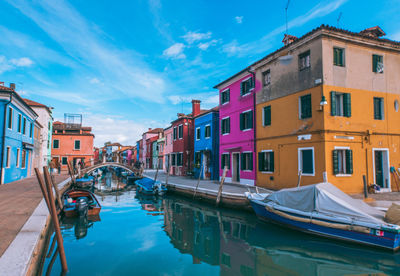 Boats moored on canal in city against sky