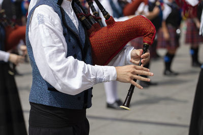 Midsection of musician playing bagpipe on street in city