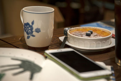 Close-up of mobile phone with creme brulee and coffee cup on table