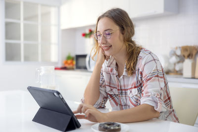 Young woman using phone while sitting on laptop