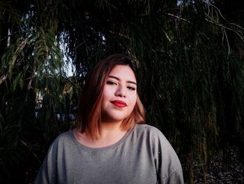 Portrait of young woman standing against tree at park