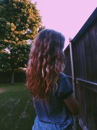 Rear view of woman standing in yard by fence against sky