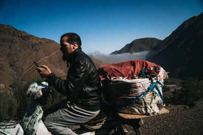 Full length of man sitting on mountain against clear sky