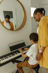 Smiling woman looking at son playing piano at home