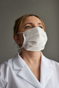 Close-up of thoughtful female doctor wearing mask looking away against gray background