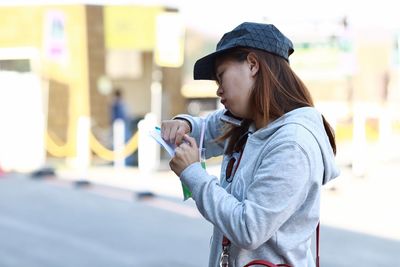 Side view of woman holding drink and paper while talking on mobile phone