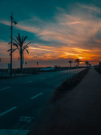 Road by silhouette city against sky during sunset