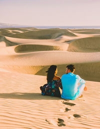 Rear view of woman sitting on sand at desert