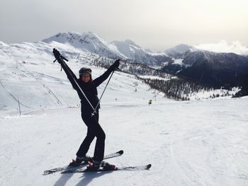 Happy woman gesturing while skiing on snowy field by mountains against sky