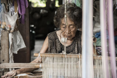 Senior woman weaving loom in factory