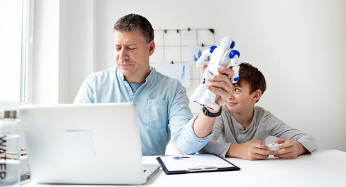 Father and son with toy and laptop on table at home