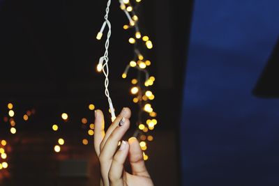 Close-up of hands holding string lights at night