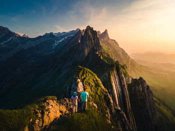 Rear view of people walking on mountain against sky during sunset