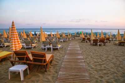Empty lounge chairs at beach during sunset