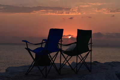 Lifeguard chair on beach against sky during sunset