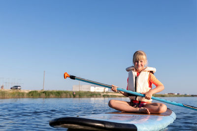 Rear view of woman kayaking in sea against clear sky