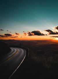 Road passing through land against sky during sunset