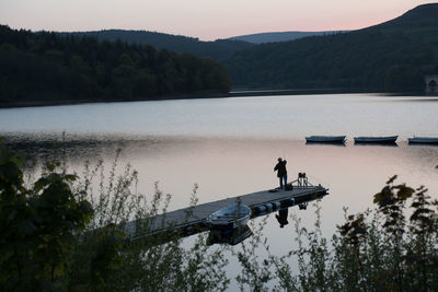 Man fishing on jetty over lake by mountains against sky