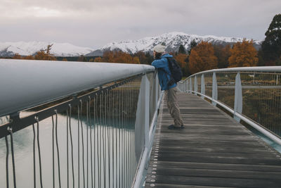 Woman looking at lake tekapo from bridge with mountains in background