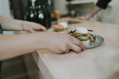 Cropped hands of woman picking plates with food from table at cafe