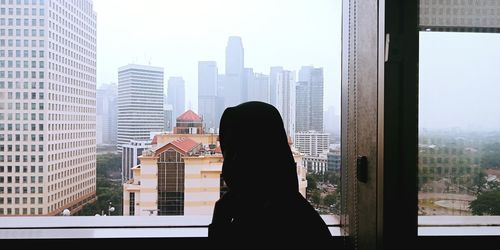 Woman looking at city buildings seen through window