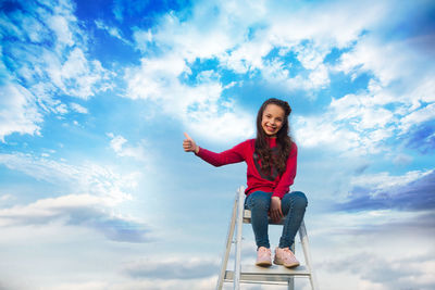 Portrait of smiling young woman sitting against sky