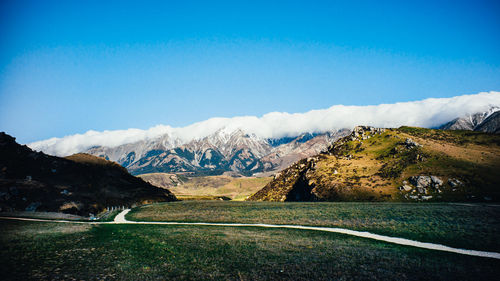 Country road leading towards mountains against blue sky