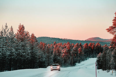 Car on snow covered road against sky during sunset