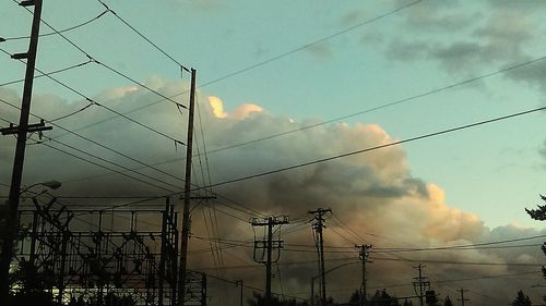 Low angle view of electricity pylon against cloudy sky