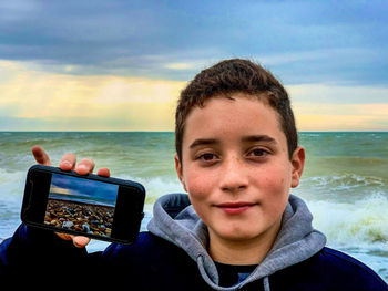 Portrait of mature man using mobile phone at beach against sky