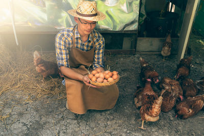 Man holding eggs in basket by chickens