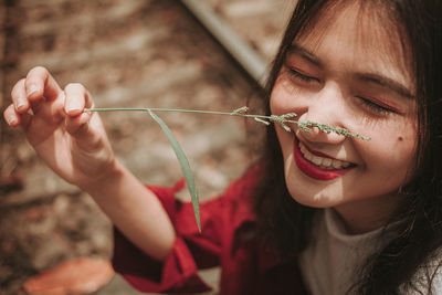 Close-up of smiling young woman holding plant on nose
