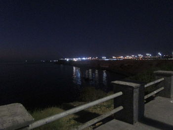 Illuminated city by sea against clear sky at night