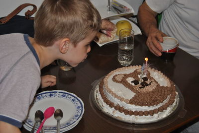High angle view of boy blowing candles at birthday cake on table