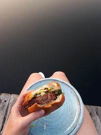 Midsection of woman holding burger while sitting on pier over lake