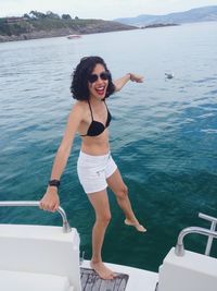 Portrait of cheerful woman standing in boat against sea