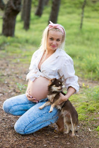 Portrait of pregnant woman with chihuahua kneeling on field at park