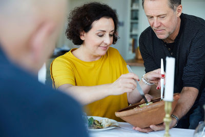 Mature man serving pasta to female friend at dining table