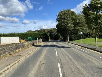 Empty road by trees against sky in city