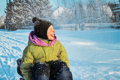 Smiling boy sitting on snow covered land during winter