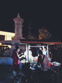 People sitting in illuminated city against clear sky at night