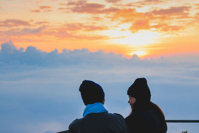 Young couple looking at view while standing on observation point against sky during sunset