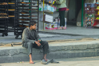 Full length of young man sitting on seat in city