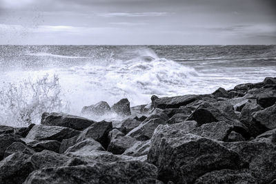 Waves splashing on rocks at shore against sky